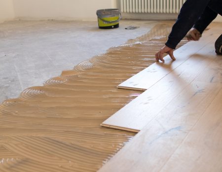 Renovation of an apartment, skilled worker uses a plastic hammer when installing pre-finished interlocking parquet. Laying with brown glue on an existing floor. Installation of oak colored parquet Renovation of an apartment, skilled worker uses a plastic hammer when installing pre-finished interlocking parquet. Laying with brown glue on an existing floor. Installation of oak colored parquet